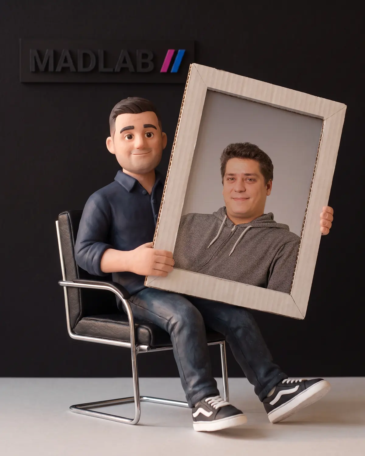 Knetfigur von Lars auf einem schwarzen Bürostuhl, mit einem Kartonrahmen und einem Foto des echten Lars