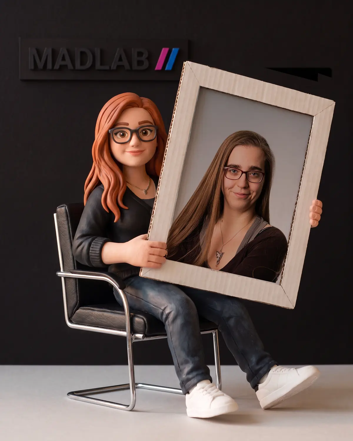 Knetfigur von Michelle auf einem schwarzen Bürostuhl, mit einem Kartonrahmen und einem Foto der echten Michelle